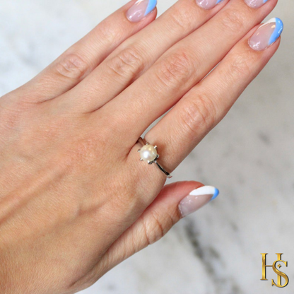 A solitaire pearl ring with a six-prong setting and a sterling silver band, worn on a hand with a blue and white manicure.