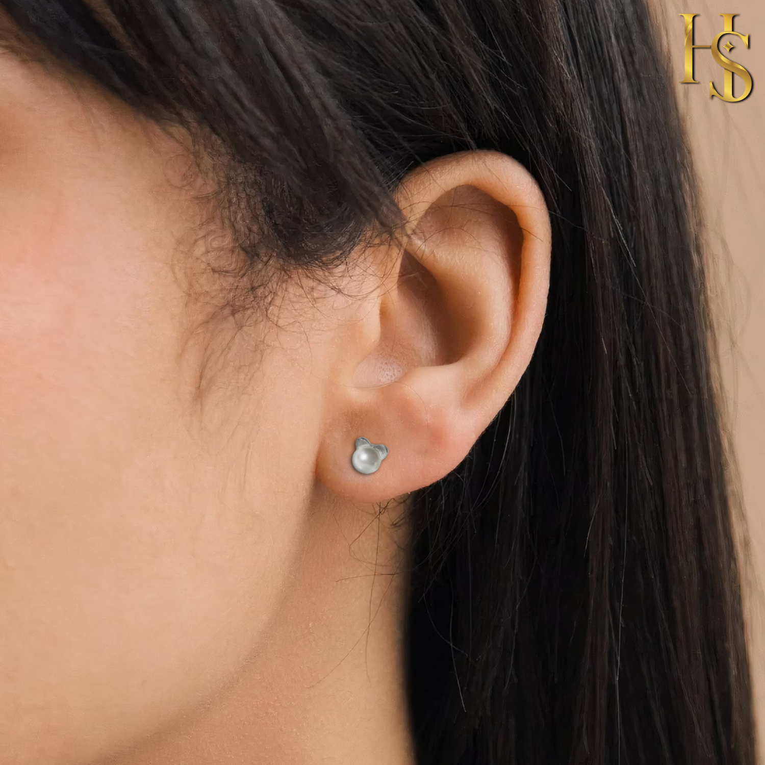 A small freshwater pearl stud earring in a sterling silver animal head setting is worn on the earlobe.