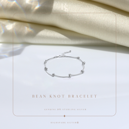 A sterling silver bracelet with polished bean-shaped knots styled on a white surface with draped cream fabric in the background.