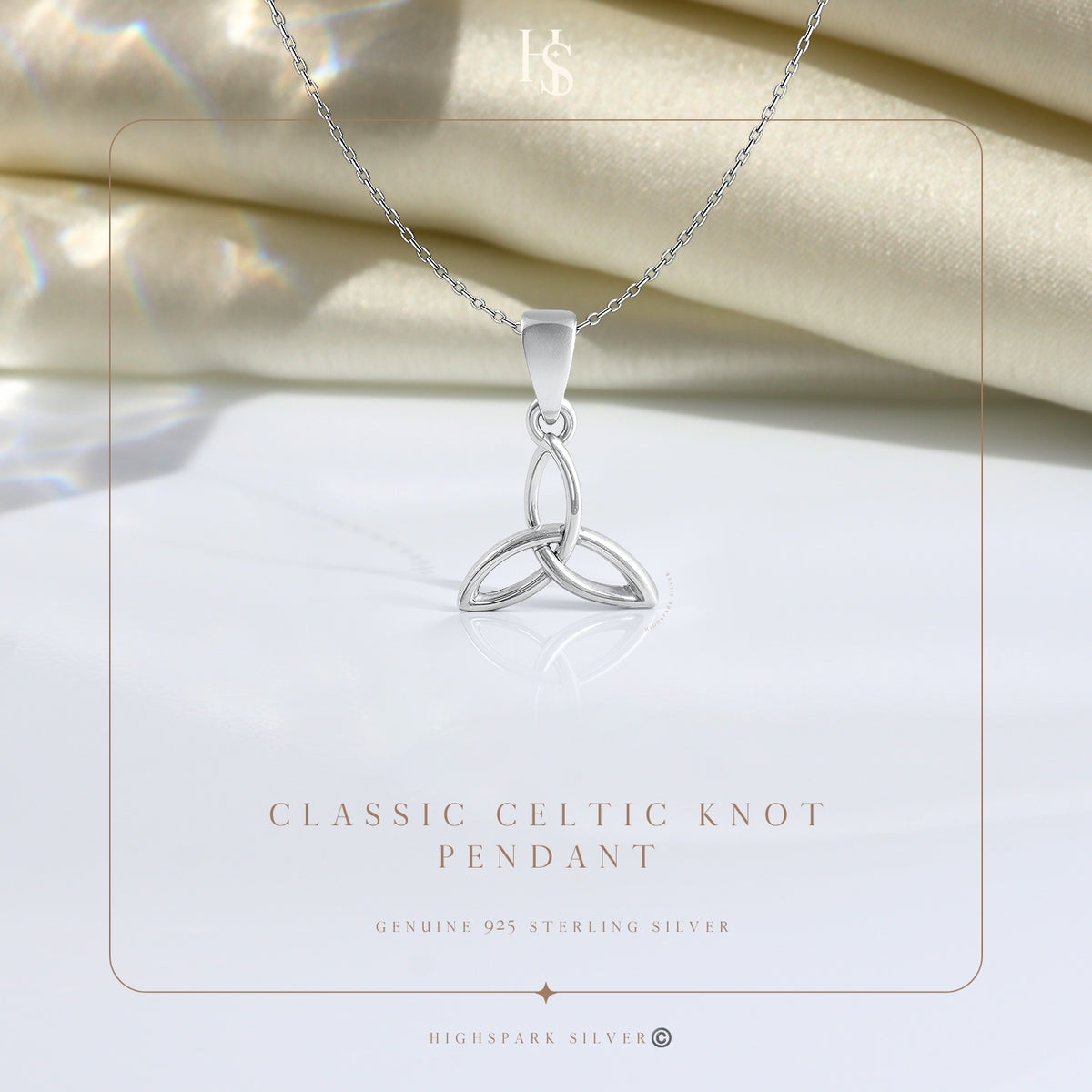 A sterling silver pendant necklace with a Celtic knot design rests on a white surface with folded cream fabric in the background.