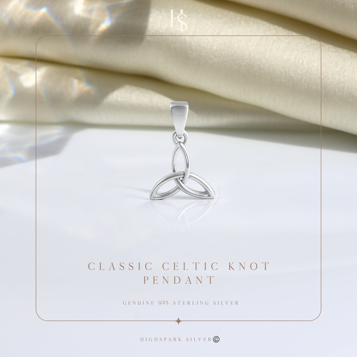 A sterling silver pendant in a Celtic knot or triquetra design, styled on a folded cream satin fabric with soft lighting.