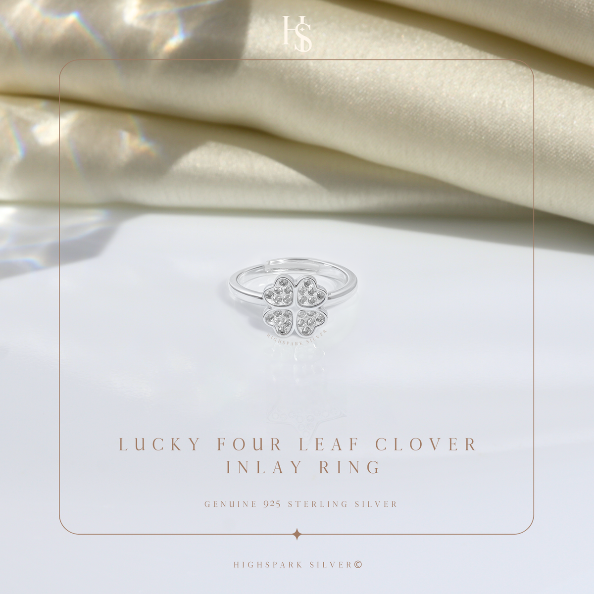 A sterling silver adjustable ring with a four-leaf clover motif paved with American diamonds, styled on a white surface with cream satin.