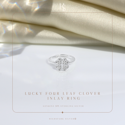 A sterling silver adjustable ring with a four-leaf clover motif paved with American diamonds, styled on a white surface with cream satin.