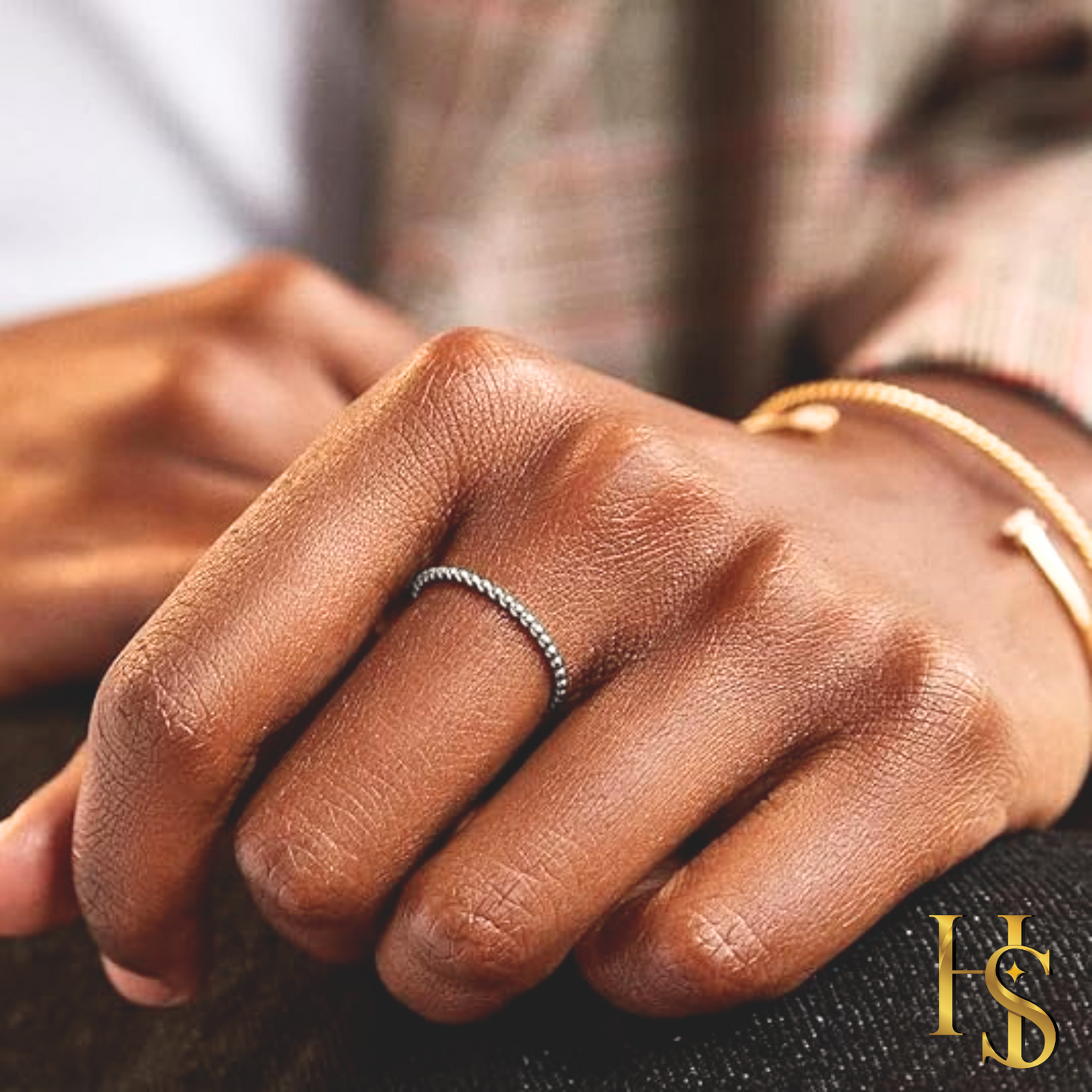 A dainty, twisted rope band ring in sterling silver worn on the finger, with a gold bracelet visible on the wrist in the background.