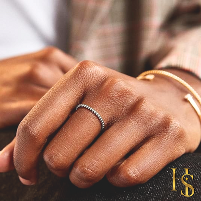 A dainty, twisted rope band ring in sterling silver worn on the finger, with a gold bracelet visible on the wrist in the background.