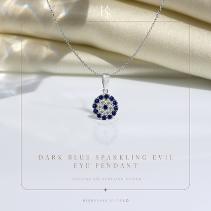 A sterling silver evil eye pendant necklace with dark blue and clear American diamonds, styled on a white surface with draped cream fabric.