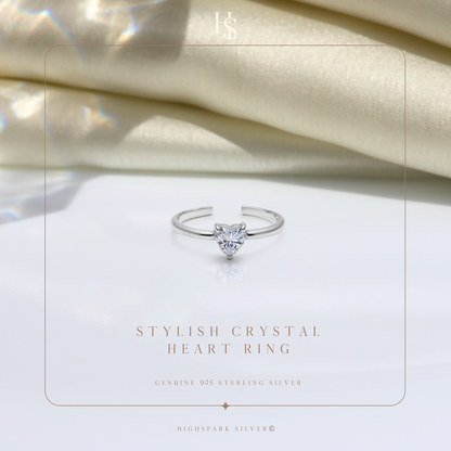 An adjustable sterling silver ring with a solitaire heart-shaped American diamond, styled on a white surface with draped cream satin fabric.