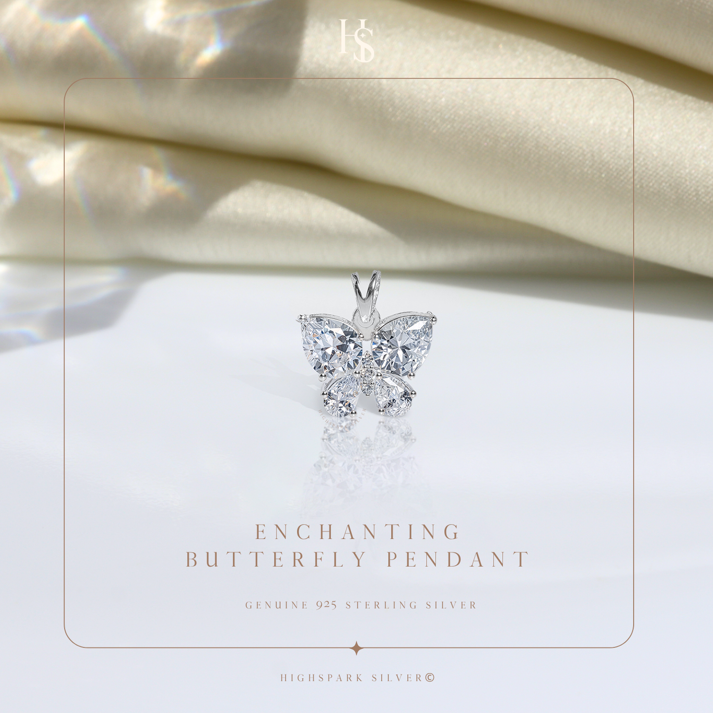 A sterling silver butterfly pendant with pear and round-cut American diamonds rests on a reflective surface with draped cream satin behind.