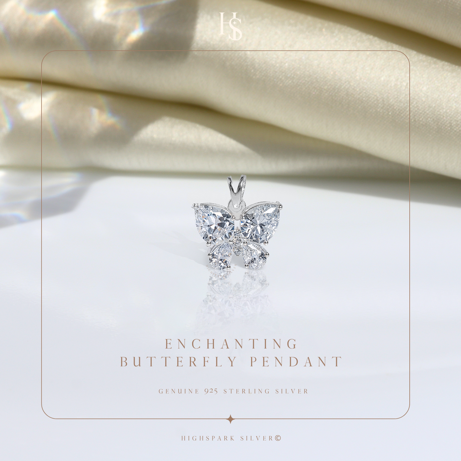 A sterling silver butterfly pendant with pear and round-cut American diamonds rests on a reflective surface with draped cream satin behind.