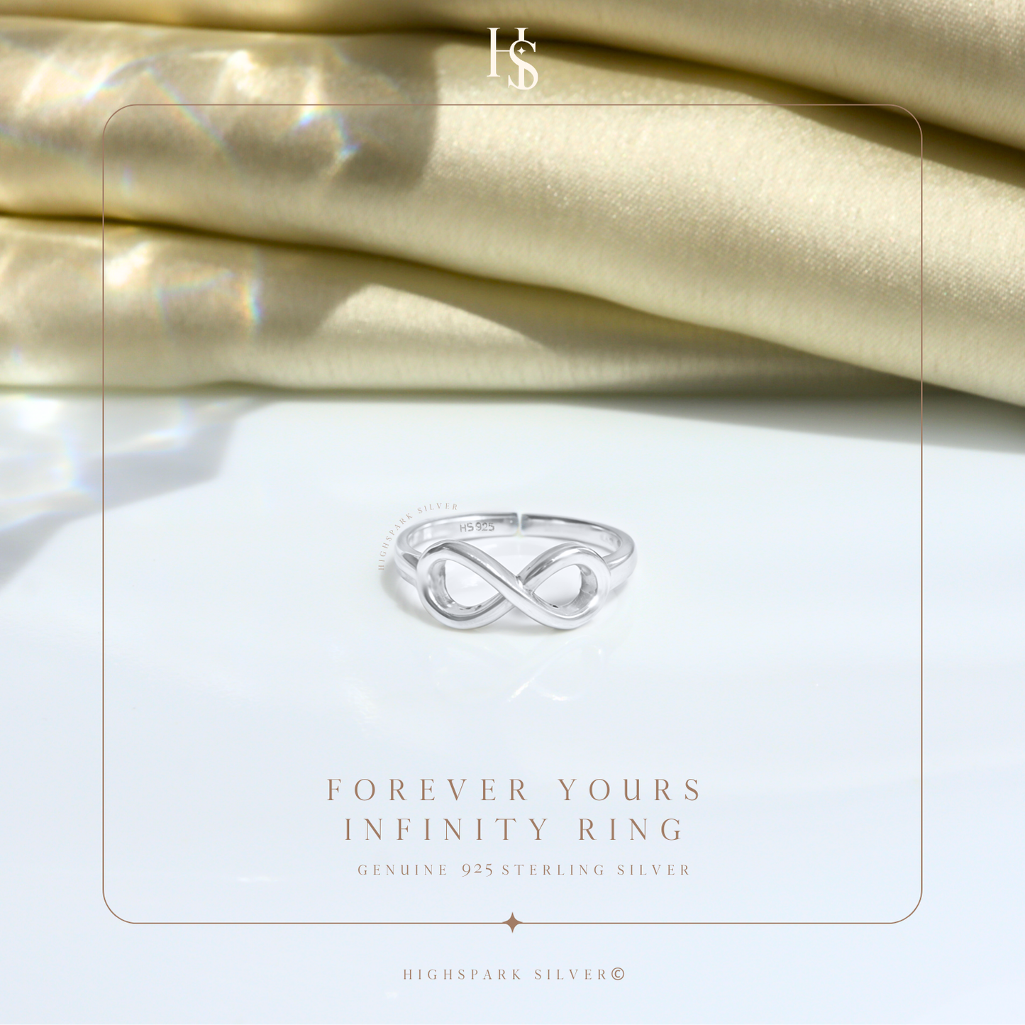 A sterling silver infinity ring with a polished finish, styled on a white surface with folded cream satin fabric in the background.