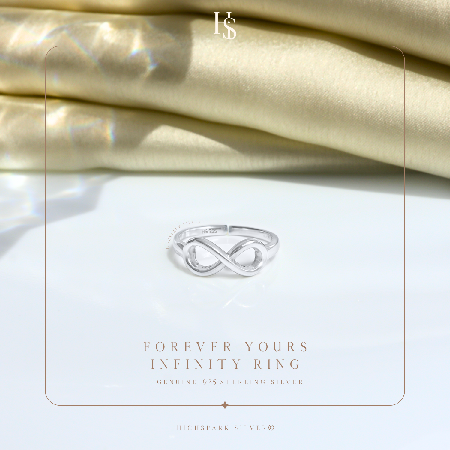 A sterling silver infinity ring with a polished finish, styled on a white surface with folded cream satin fabric in the background.