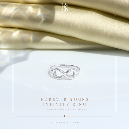 A sterling silver infinity ring with a polished finish, styled on a white surface with folded cream satin fabric in the background.
