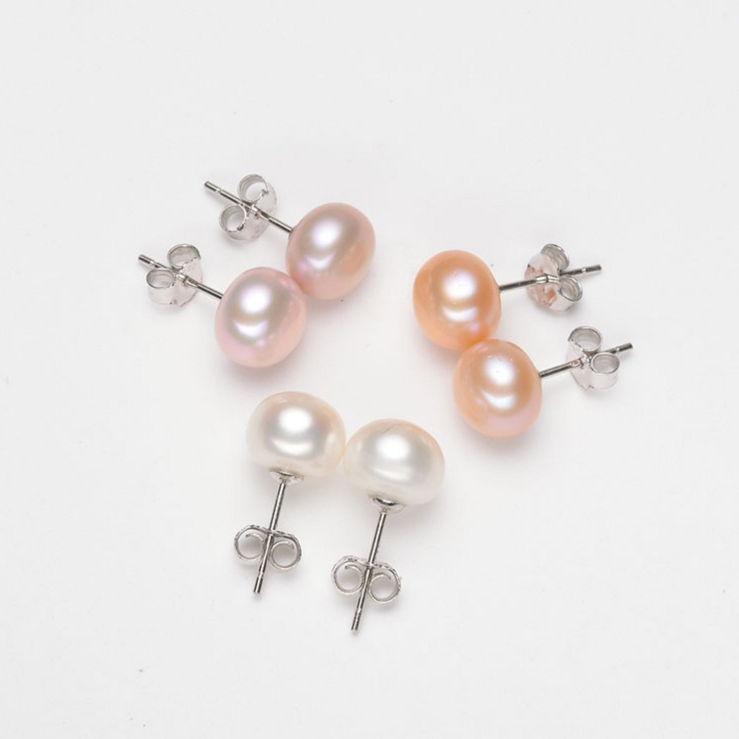 Three pairs of oval freshwater pearl stud earrings in white, pink, and peach with sterling silver posts, shown on a white background.