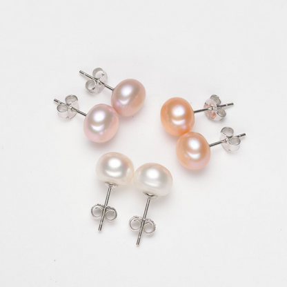 Three pairs of oval freshwater pearl stud earrings in white, pink, and peach with sterling silver posts, shown on a white background.