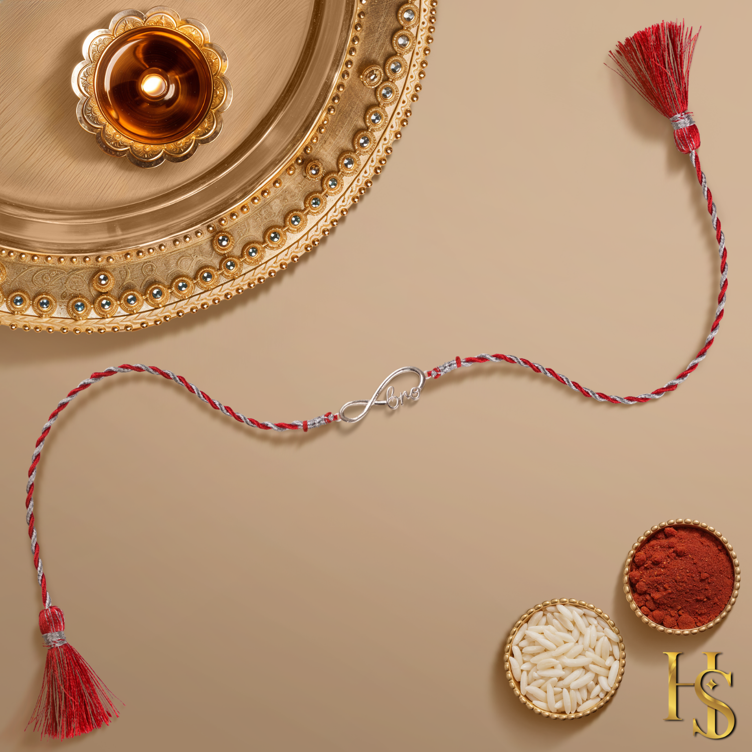 A 925 sterling silver rakhi for brother with an infinity 'bro' motif on a red and silver twisted thread, shown with a pooja thali.