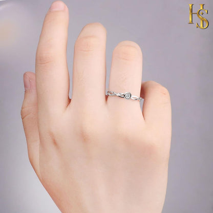 A sterling silver ring with an intertwined band and a single bezel-set American diamond worn on a finger.