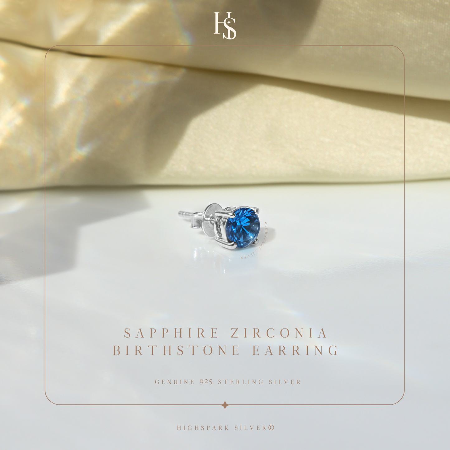 A single sterling silver stud earring with a round sapphire blue stone in a four-prong setting, styled on a reflective white surface.