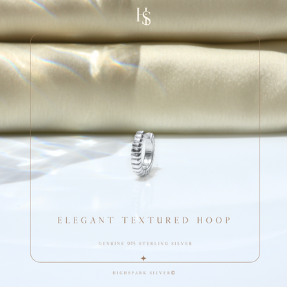A single sterling silver huggie hoop earring with a ribbed texture.