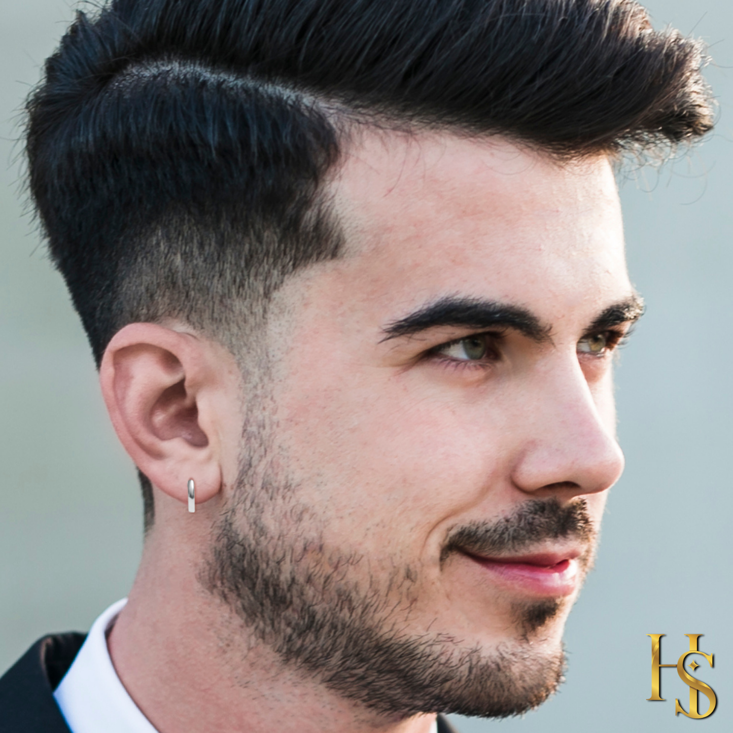 A small, minimalist sterling silver half hoop earring worn on a man's earlobe against a blurred background.
