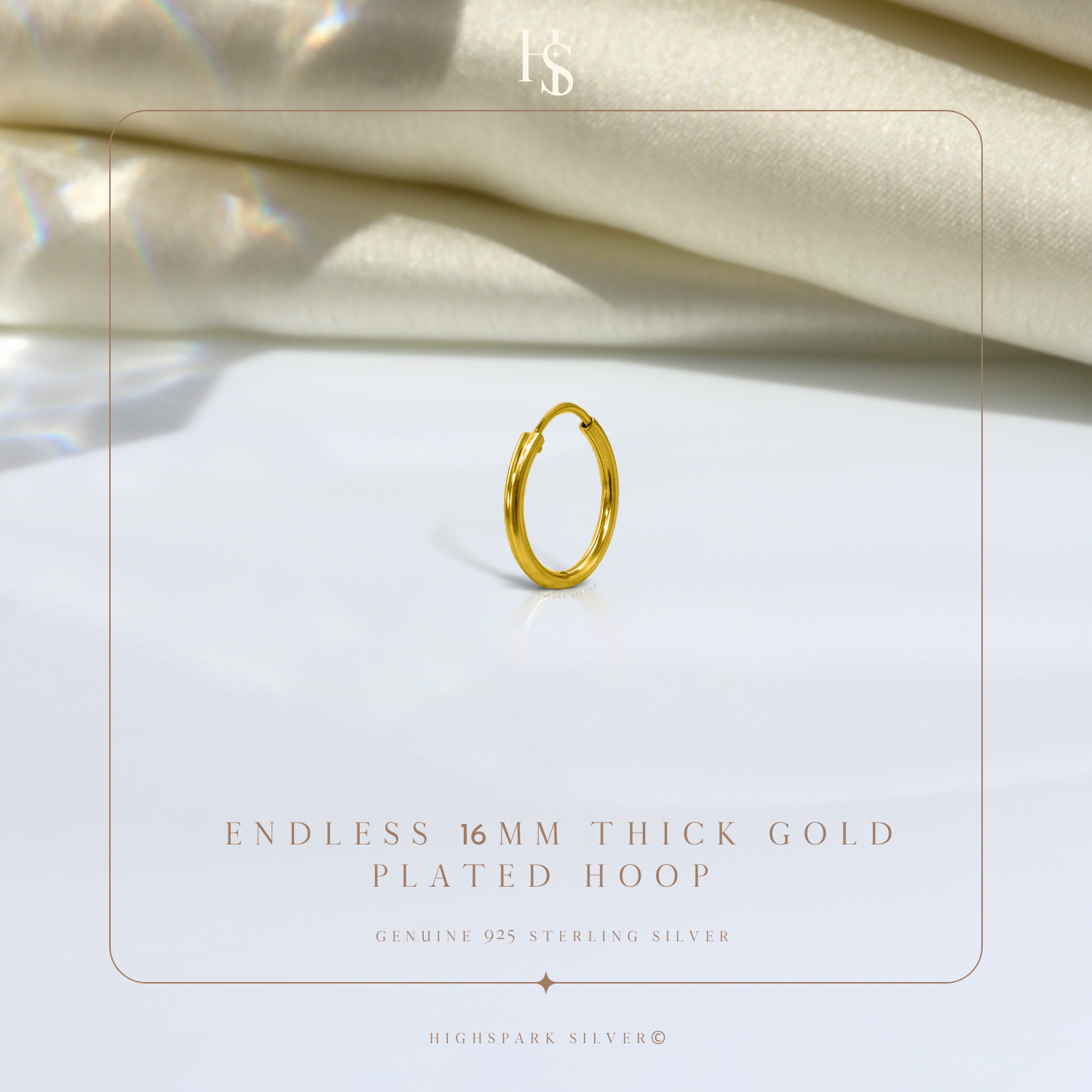A single gold-plated sterling silver endless hoop earring styled on a white surface with draped cream fabric in the background.