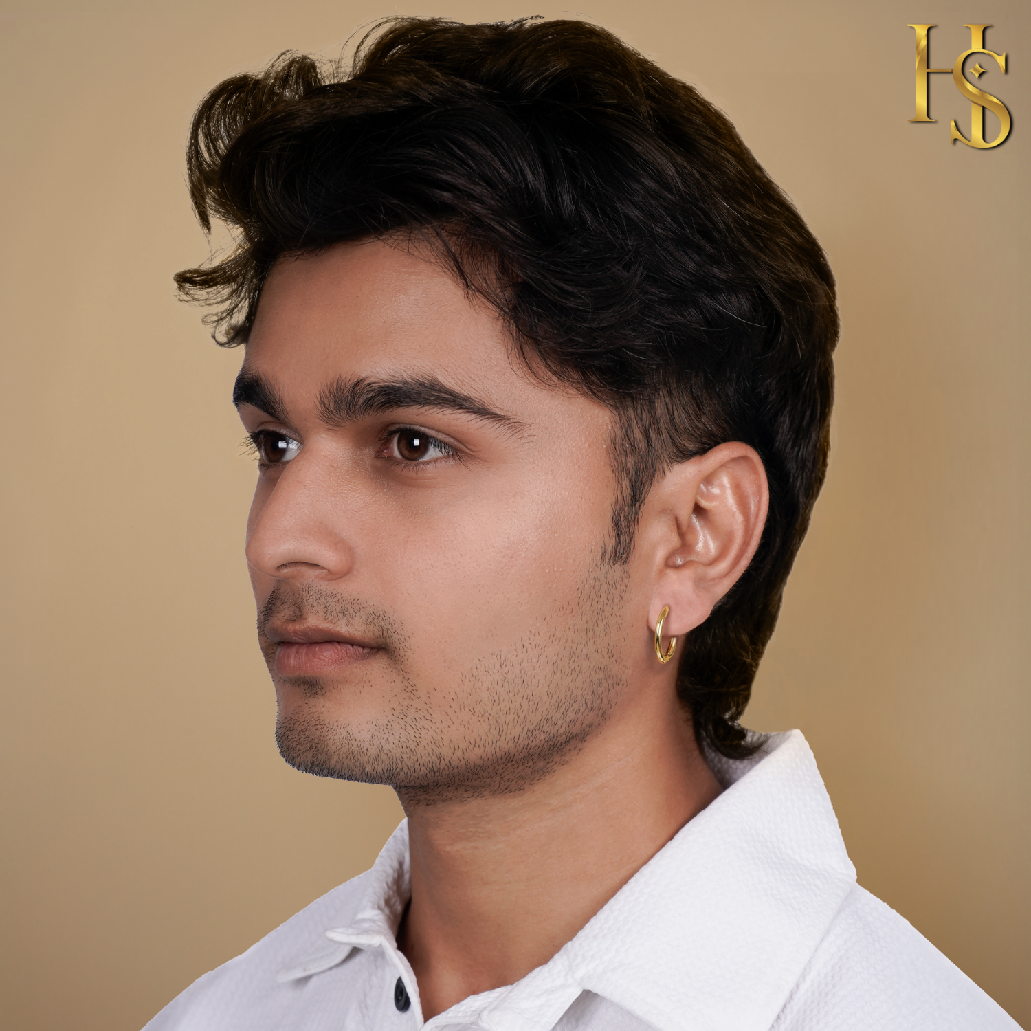 A small, classic gold-plated hoop earring worn on a man's ear against a plain beige background.