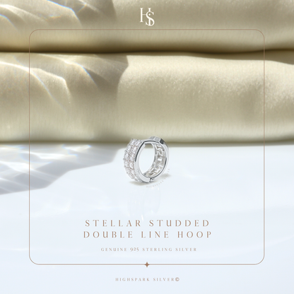 A sterling silver huggie hoop earring with two rows of pavé-set American diamonds, styled on a white surface with folded beige fabric.