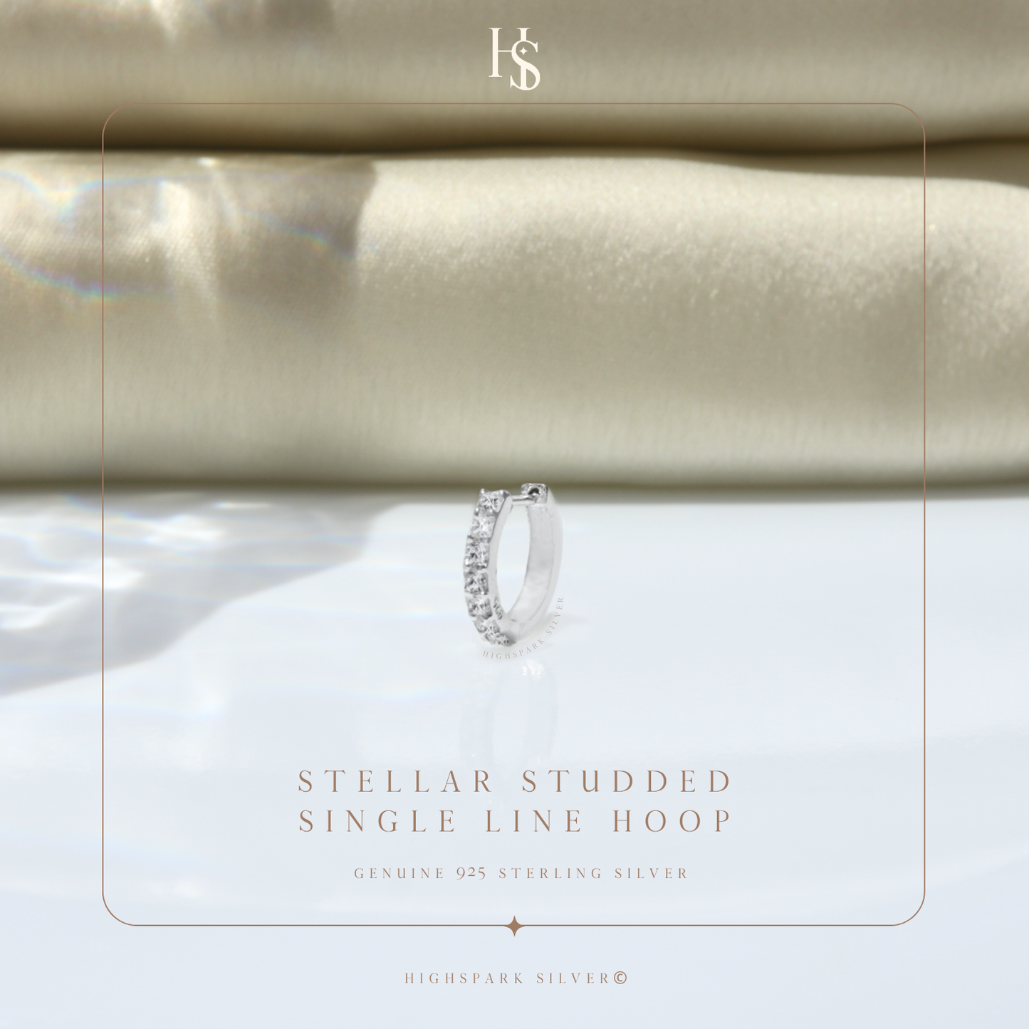 A single sterling silver hoop earring with a row of channel-set American diamonds, styled on a reflective surface with folded cream fabric.