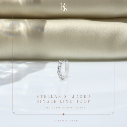 A single sterling silver hoop earring with a row of channel-set American diamonds, styled on a reflective surface with folded cream fabric.