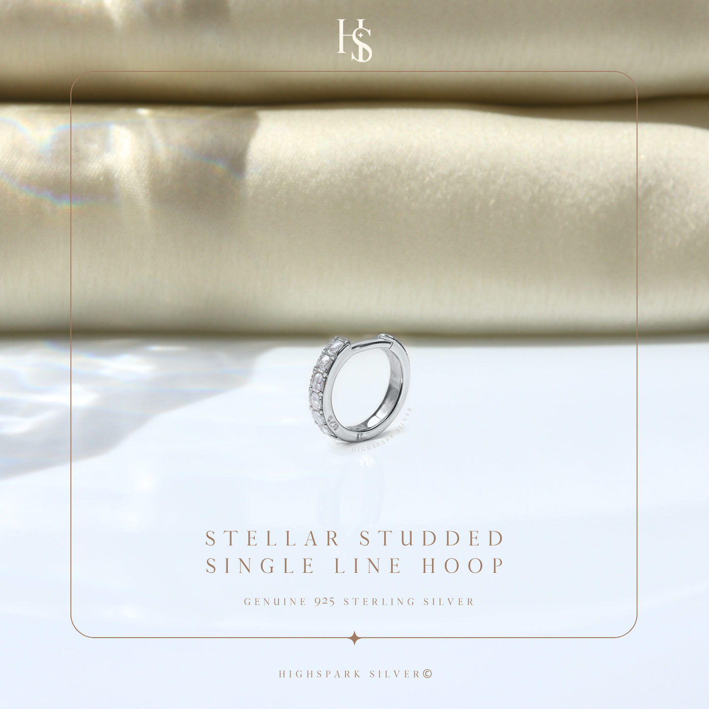 A single sterling silver hoop earring with a line of channel-set American diamonds, styled on a reflective surface with soft fabric.