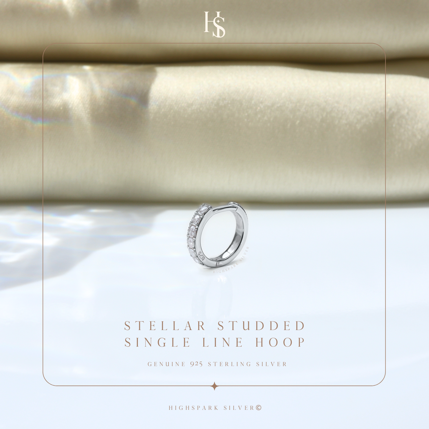 A single sterling silver hoop earring with a line of channel-set American diamonds, styled on a reflective surface with soft fabric.