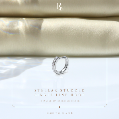 A single sterling silver hoop earring with a line of channel-set American diamonds, styled on a reflective surface with soft fabric.