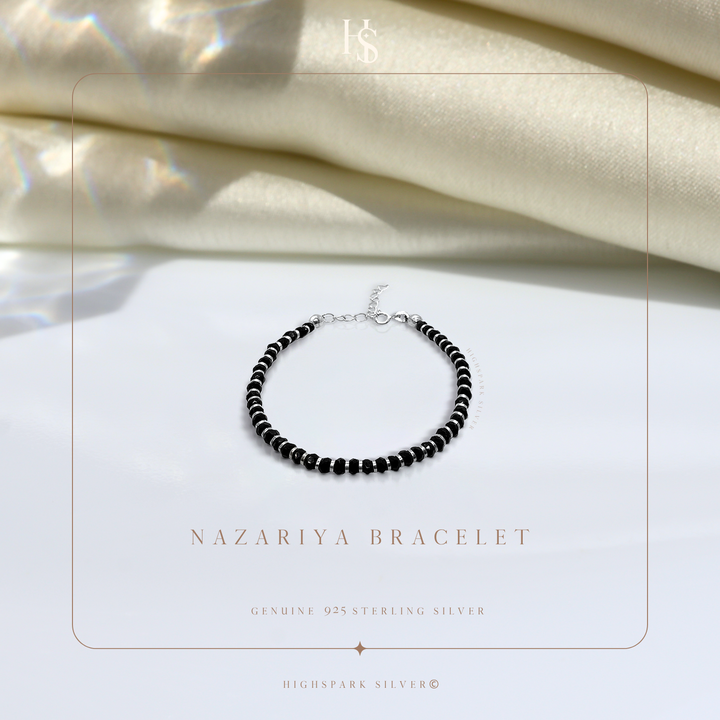 A nazariya bracelet with tiny black beads and sterling silver accents, styled on a white surface with draped ivory satin in the background.