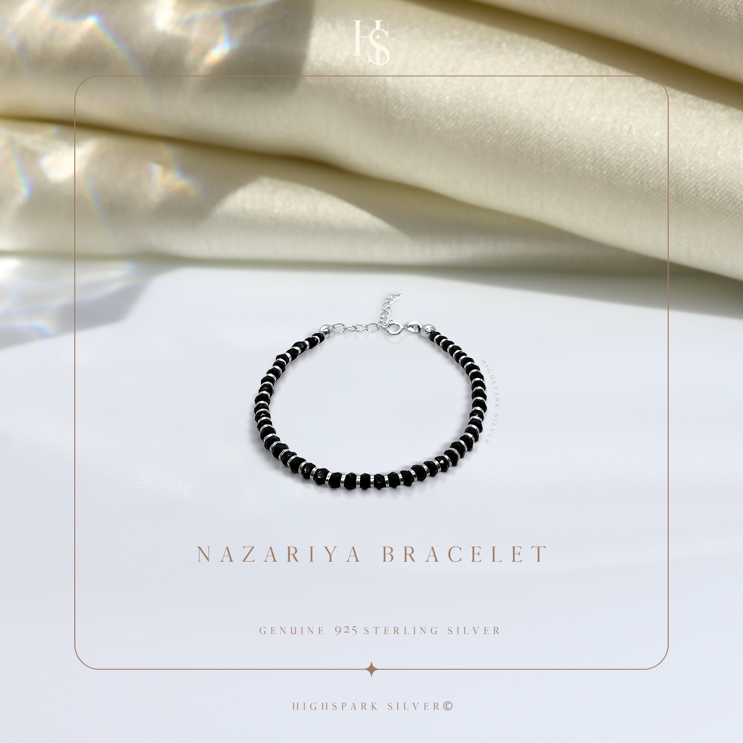 A nazariya bracelet with tiny black beads and sterling silver accents, styled on a white surface with draped ivory satin in the background.