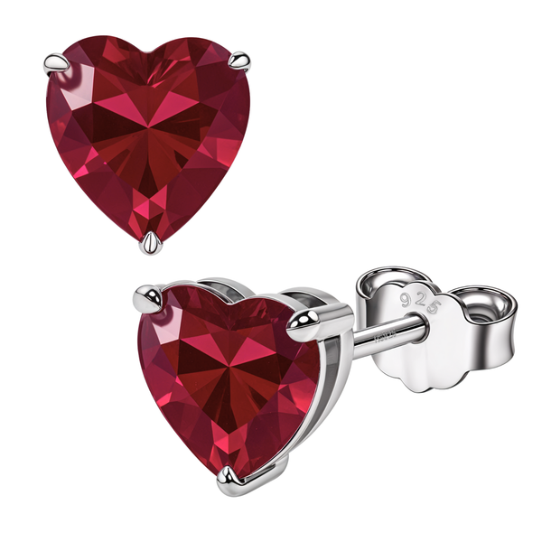 A pair of heart-shaped stud earrings with a faceted red gemstone in a three-prong sterling silver setting on a white background.