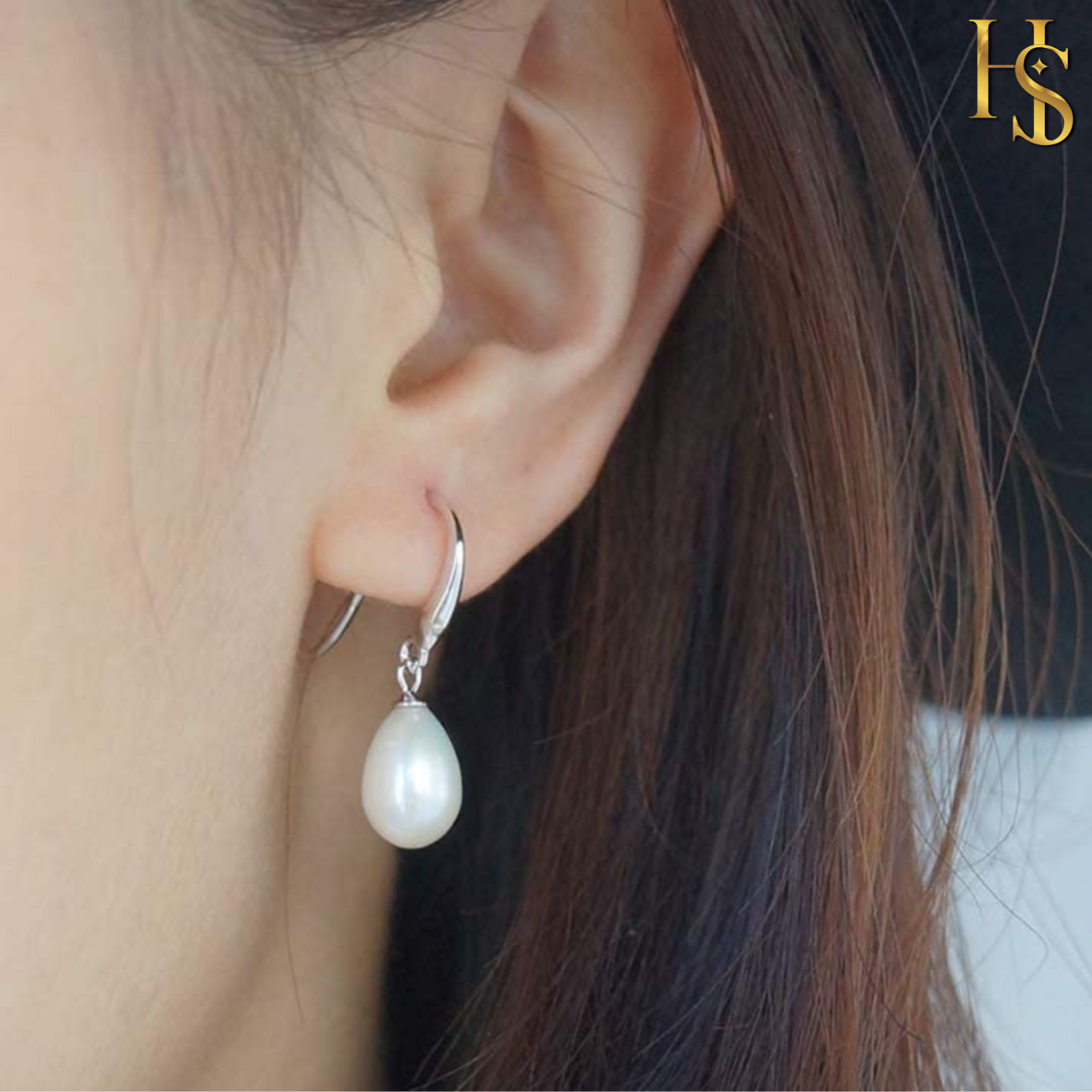 A teardrop pearl drop earring with a lever-back hook in sterling silver, worn on the ear.