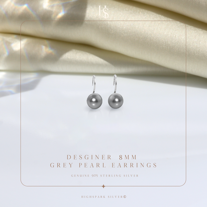 A pair of sterling silver hook earrings with round grey pearls, styled on a white surface with draped cream satin in the background.
