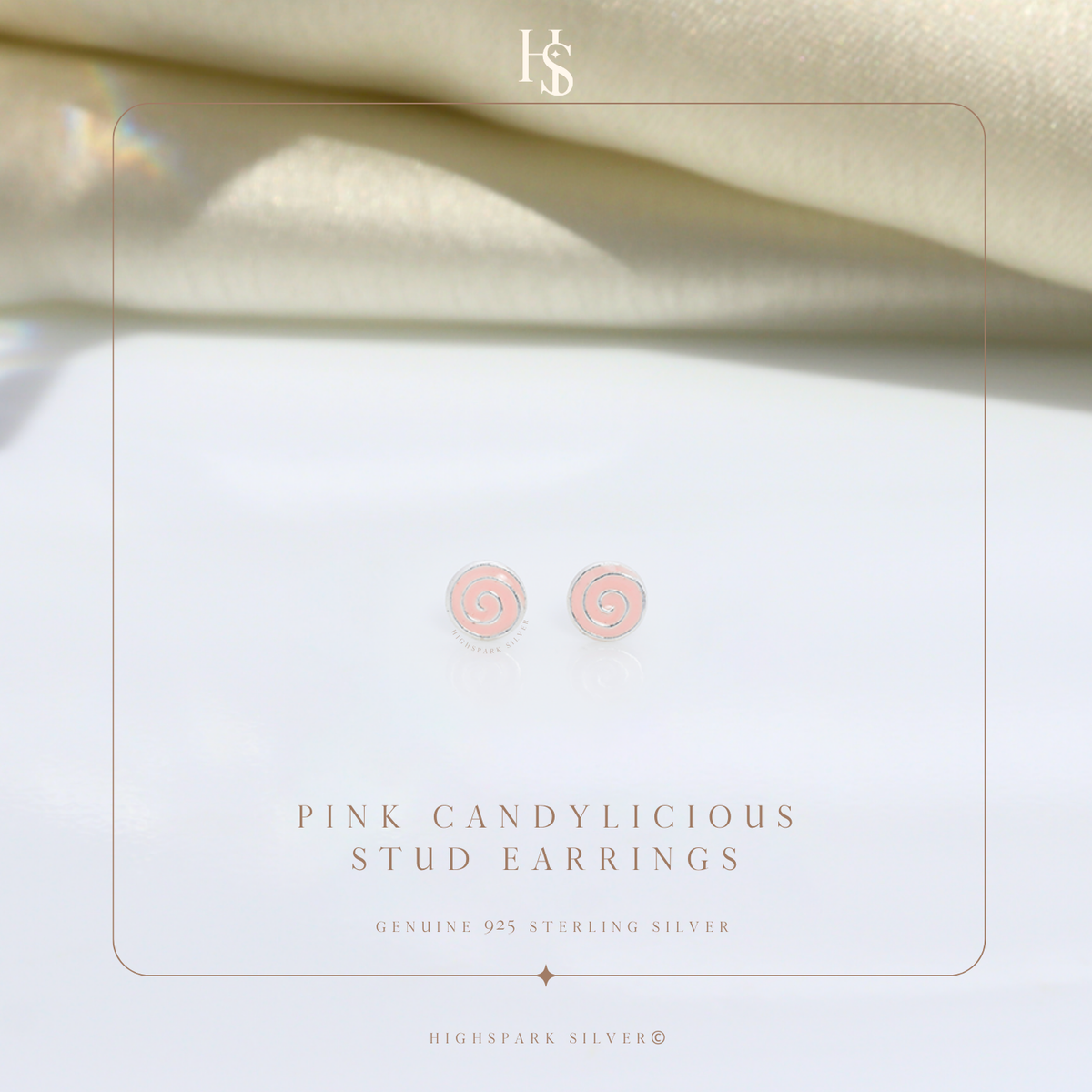 A pair of sterling silver stud earrings with a pink enamel swirl design, styled on a white surface with draped cream fabric.