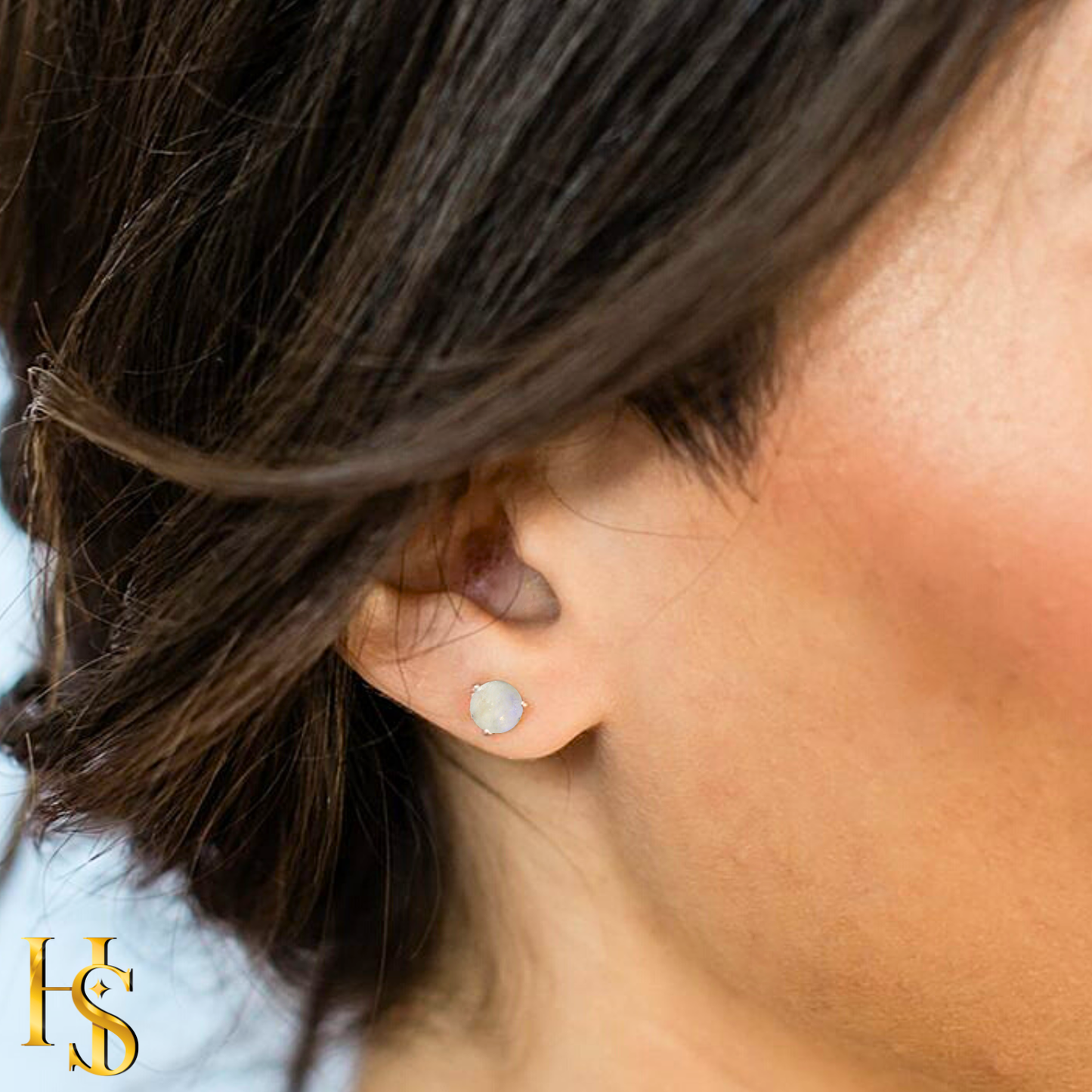 A round moonstone stud earring in a sterling silver prong setting, worn on the ear of a model with dark hair.