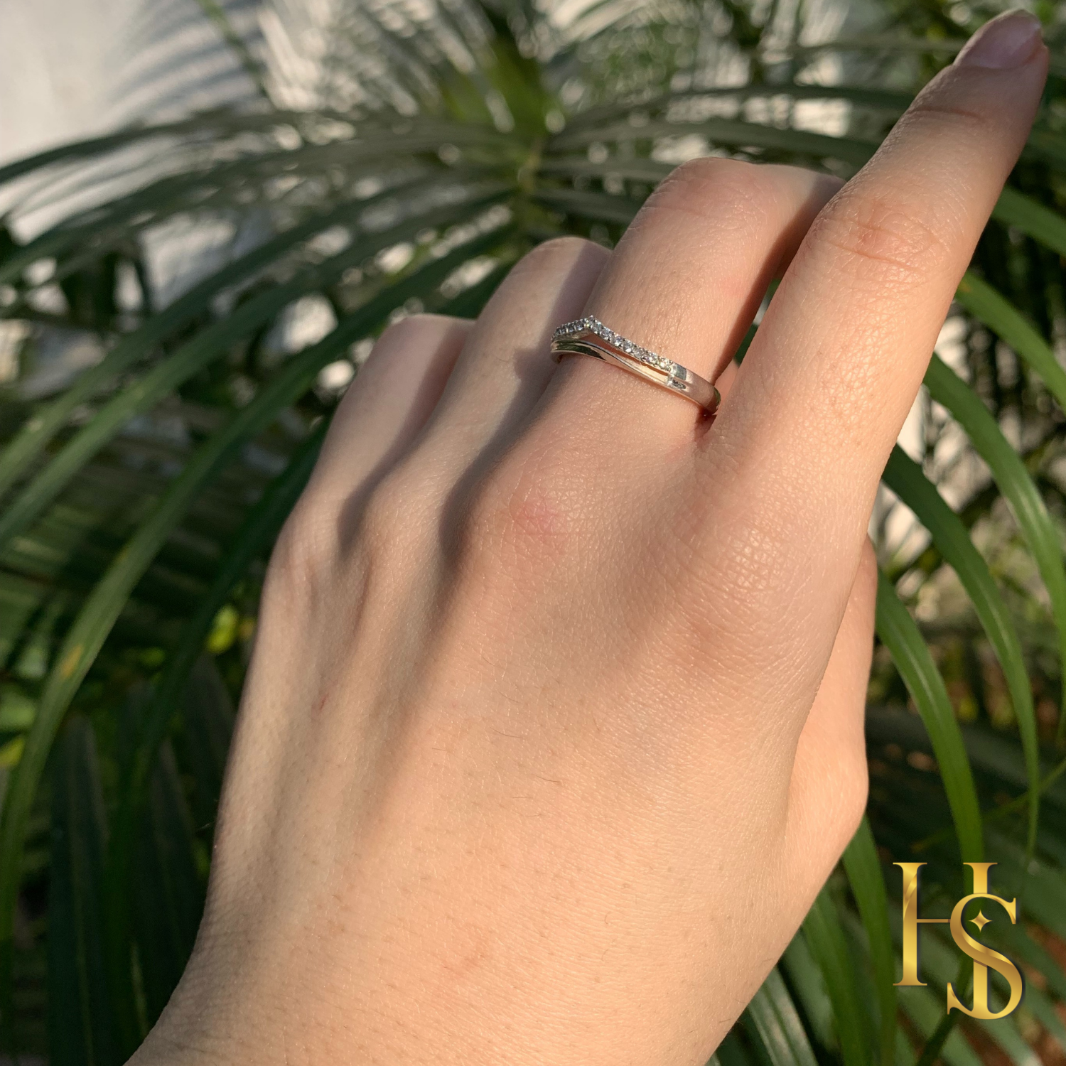 A sterling silver crown ring with pavé-set American diamonds worn on a hand in front of green palm leaves.