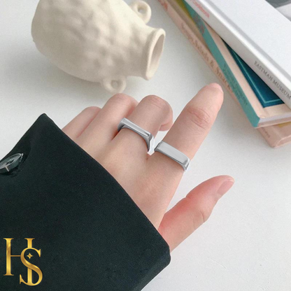 Two minimalist sterling silver signet band rings worn on a hand, styled with a black sleeve, books, and a white vase in the background.