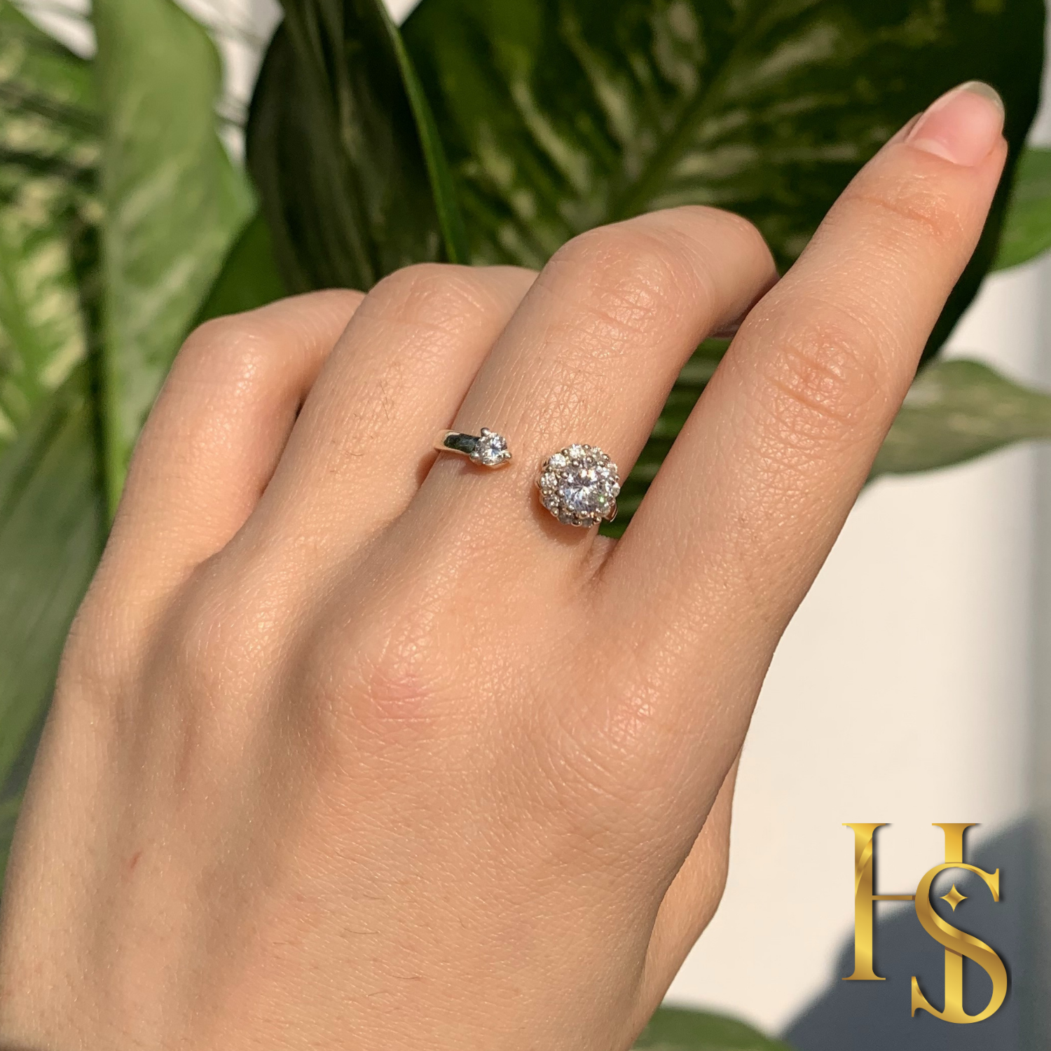 An adjustable sterling silver ring with a floral American diamond cluster and a single solitaire worn on a hand against a leafy background.