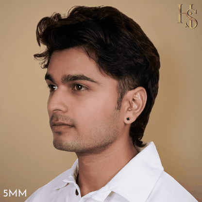 A round black solitaire stud earring in a sterling silver setting worn on a man's ear against a solid beige background.