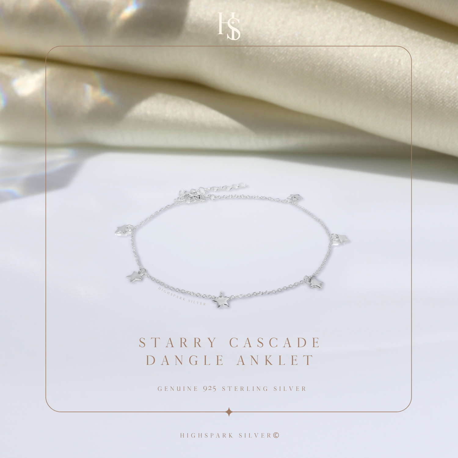 A sterling silver anklet with small dangling star charms, styled on a white surface with draped cream fabric in the background.