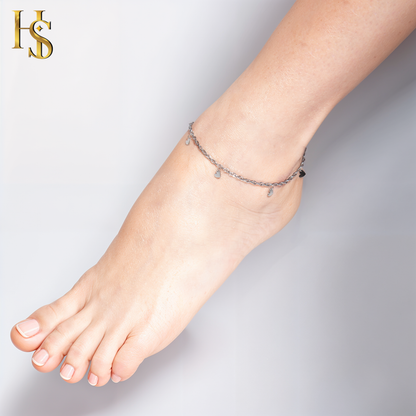 A sterling silver chain anklet with small, dangling heart charms is worn on a model's ankle against a plain background.