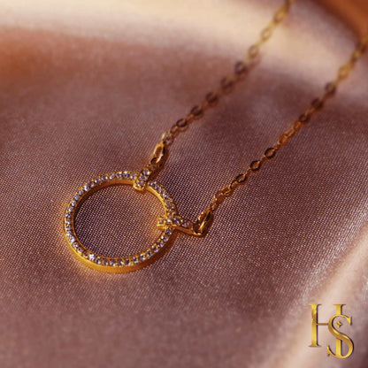 A gold-plated sterling silver necklace with a circular pendant studded with American diamonds, styled on a folded pink satin fabric.
