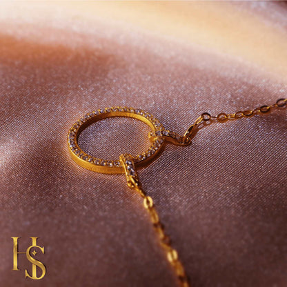 A gold-plated pendant necklace with a circular motif paved with American diamonds, styled on a shimmering rose-gold satin fabric.