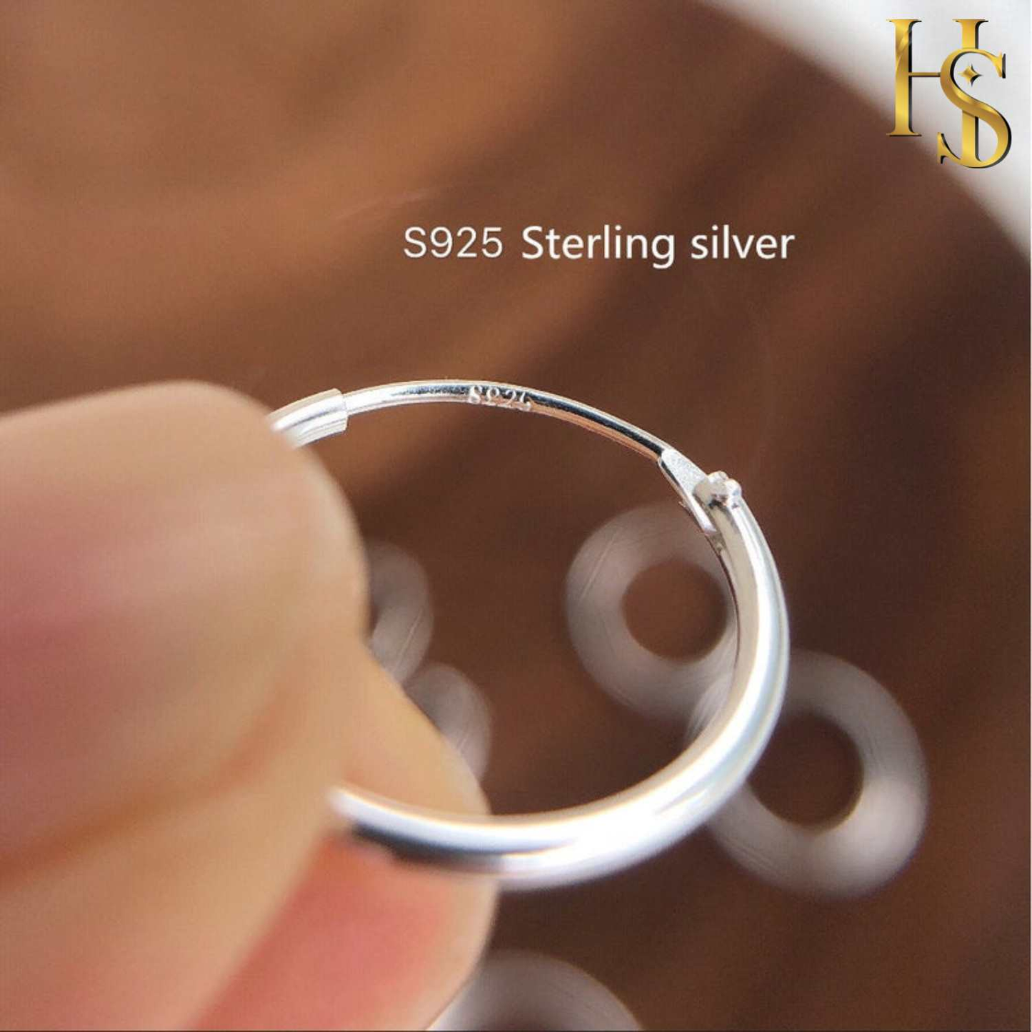 A closeup of a classic sterling silver hoop earring held between two fingers, showing the wire clasp and the 925 hallmark stamp.