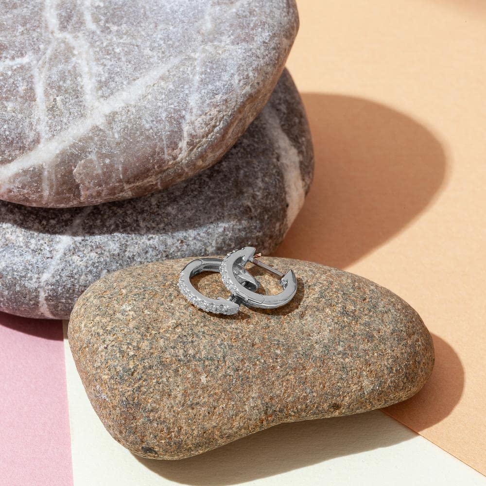 A pair of sterling silver hoop huggie earrings with pave-set American diamonds resting on smooth river stones.