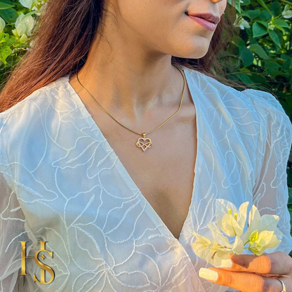 A gold-plated pendant necklace with an infinity symbol inside a heart, studded with American diamonds, worn on the neck with a white dress.