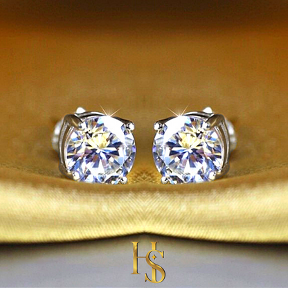A pair of solitaire stud earrings with round American diamonds in a four-prong setting, styled on a folded golden-yellow satin fabric.